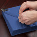 A person wrapping silverware in a navy blue Creative Converting luncheon napkin.