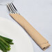 A fork and knife wrapped in a Creative Converting glittering gold napkin on a plate.