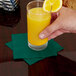 A hand holding a glass of orange juice with a Creative Converting Hunter Green beverage napkin.