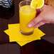 A hand holding a glass of orange juice with a School Bus Yellow beverage napkin.