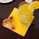 A glass of orange juice with pastries on a School Bus Yellow Creative Converting beverage napkin.