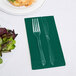 A fork and knife on a hunter green napkin next to a plate of salad.
