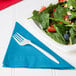 A plate of salad with a fork and a turquoise Creative Converting luncheon napkin.