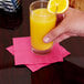 A person holding a glass of hot magenta pink beverage napkin with a slice of lemon over a table with a lemon and a glass of orange juice.