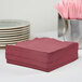 A stack of burgundy Creative Converting 1/4 fold luncheon napkins on a table.
