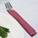 Burgundy luncheon napkin wrapped around a fork and knife on a plate.