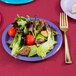 A plate of salad on a purple paper plate with a fork and knife.