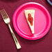 A slice of cheesecake with strawberry jam on a hot magenta pink Creative Converting paper plate with a fork.