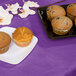 A Creative Converting amethyst purple table cover on a table with a plate of muffins.