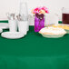 A table with Creative Converting Emerald Green OctyRound table cover, plates, and cups on it.