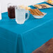 A turquoise blue Creative Converting plastic table cover on a table with food and drinks.