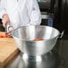 A chef uses a Vollrath aluminum colander to rinse tomatoes.