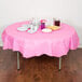 A table with a pink Creative Converting octyround tablecloth, plates, and cups with food on it.