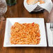 A Libbey white square porcelain pasta bowl filled with spaghetti and sauce on a table.