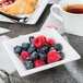 A Libbey ultra bright white square porcelain bowl filled with blueberries and raspberries on a table.