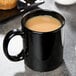 A black Libbey porcelain mug filled with a brown liquid on a table.