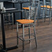 A Lancaster Table & Seating clear coat finish cross back bar stool with a cherry wood seat on a table in a restaurant.