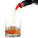 A Tablecraft red liquor pourer pouring red liquid into a glass of ice.