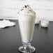 A glass of Ghirardelli White Mocha Frappe Mix milkshake with whipped cream on a table.