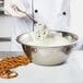 A person in a white chef's coat mixing pretzels into a bowl of Ghirardelli White Coating Wafers.