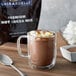 A glass mug of Ghirardelli hot chocolate with marshmallows and a spoon.