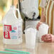 A gallon jug of Carnival King neutral slush syrup concentrate next to two cups of shaved ice.