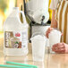 A gallon jug of Carnival King coconut slush syrup concentrate next to two cups of shaved ice with dome lids.