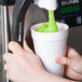 A person pouring green Carnival King Lemon Lime Slushy concentrate into a cup.