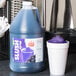 A jug of Carnival King grape slushy syrup next to a cup of purple slush.