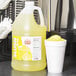 A jug of Carnival King lemon slushy syrup next to a cup of slushy.