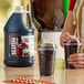 A gallon jug of Carnival King root beer slush syrup concentrate next to two cups of prepared root beer slushies.