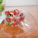 A Dart clear plastic bowl with strawberries and lettuce in it.