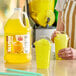 A gallon jug of Carnival King banana slush syrup concentrate next to two cups of yellow banana slushies.