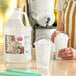 A one-gallon jug of Carnival King coconut slush syrup concentrate next to two cups of shaved ice.