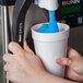 A person pouring blue Carnival King Blue Raspberry Slushy concentrate into a white cup.