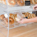 A person putting bagels in a glass bakery display case with front doors.
