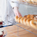 A person putting bagels in a Vollrath bakery display case with front and rear doors.