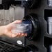 A person holding a plastic cup in a Vollrath countertop cup dispenser.