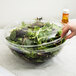 A hand holding a clear Fineline PET plastic bowl filled with green and red salad.