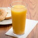 A Cambro clear plastic tumbler filled with orange juice next to a plate of bagels.