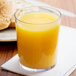 A Cambro clear plastic tumbler filled with orange juice on a table next to bread.