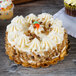 A 6 inch cake with white frosting and nuts on a gold cake circle.