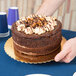 A round chocolate cake with cream and nut topping placed on a gold laminated corrugated cake circle.
