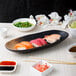 A 10 Strawberry Street Whittier Nagoya oval stoneware platter holding sushi on a table.