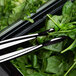 Thunder Group black polycarbonate tongs holding a bunch of spinach.