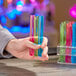 A hand holding Choice neon test tubes filled with colorful liquid.