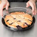 A person holding a pie in a black plastic container with a clear lid.