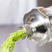 A Hamilton Beach wheatgrass juicer spraying green juice into a metal container.
