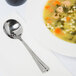 A Libbey stainless steel bouillon spoon in a bowl of soup on a white plate.