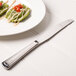 A Libbey stainless steel dinner knife on a plate of food with tomatoes and cheese.